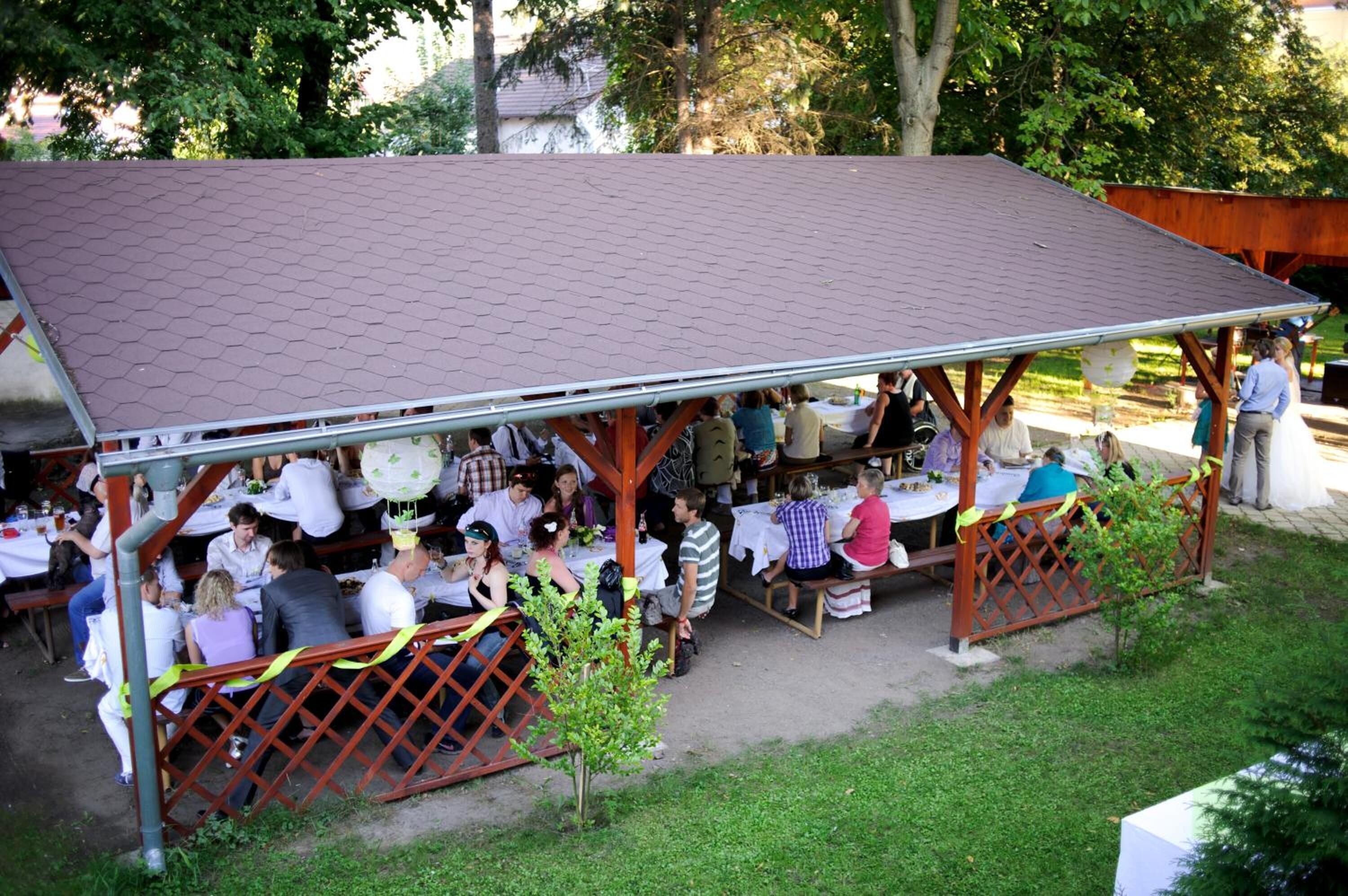 An outdoor covered dining area with tables and chairs, surrounded by greenery.