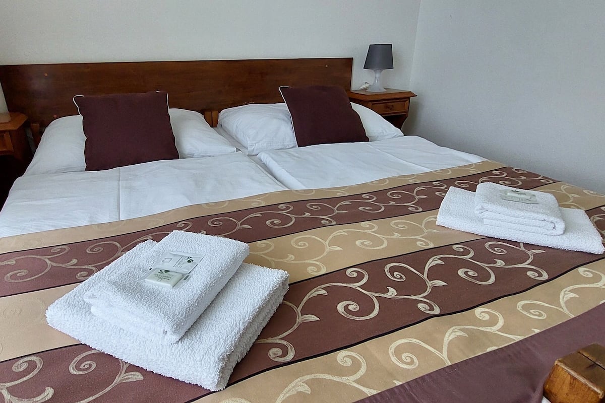 Una cama bien hecha con un edredón estampado, dos almohadas y dos toallas dobladas sobre la cama.