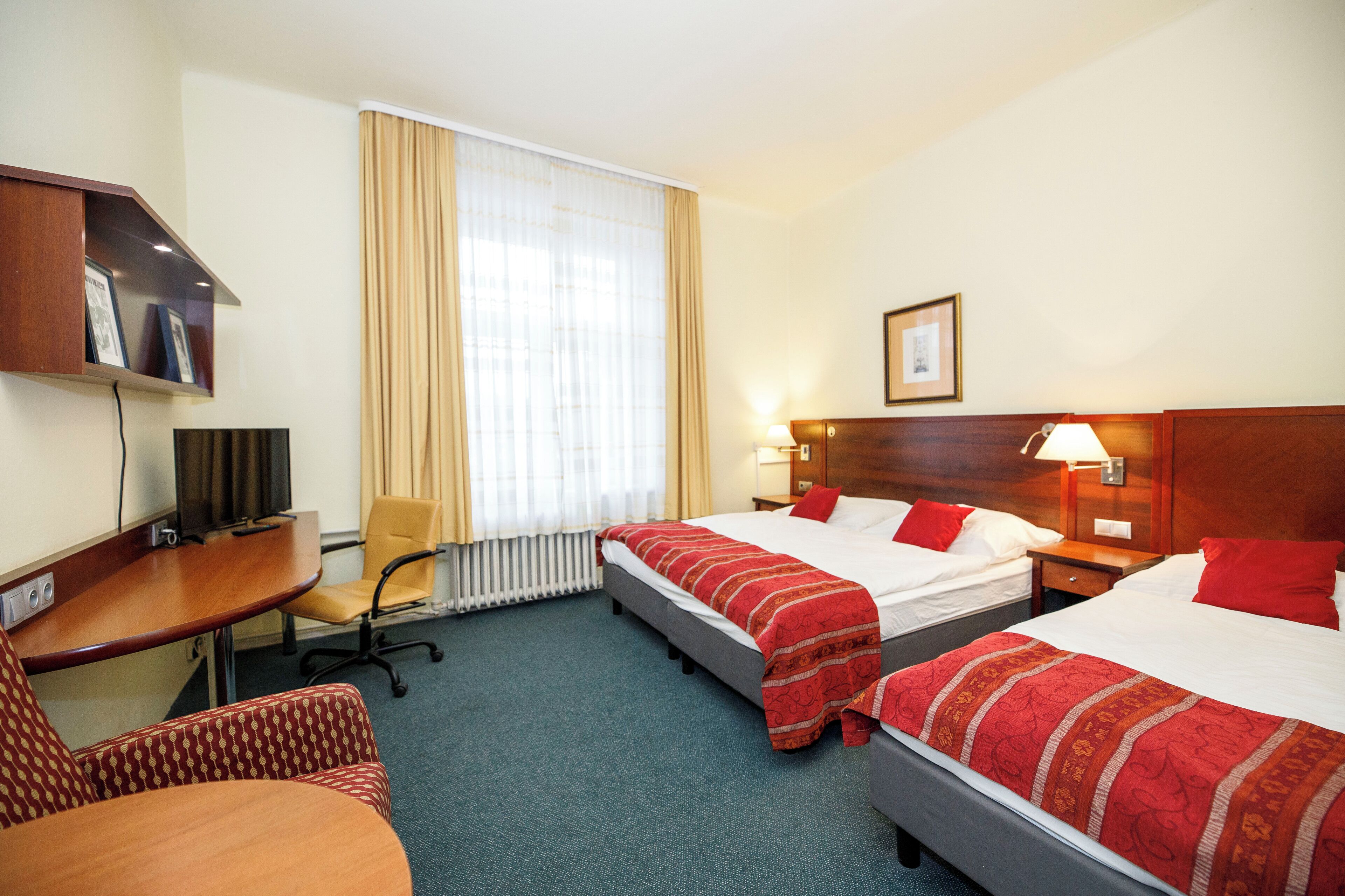 Ein Hotelzimmer mit zwei Betten, einem Schreibtisch, einem Sessel und einem Fernseher.