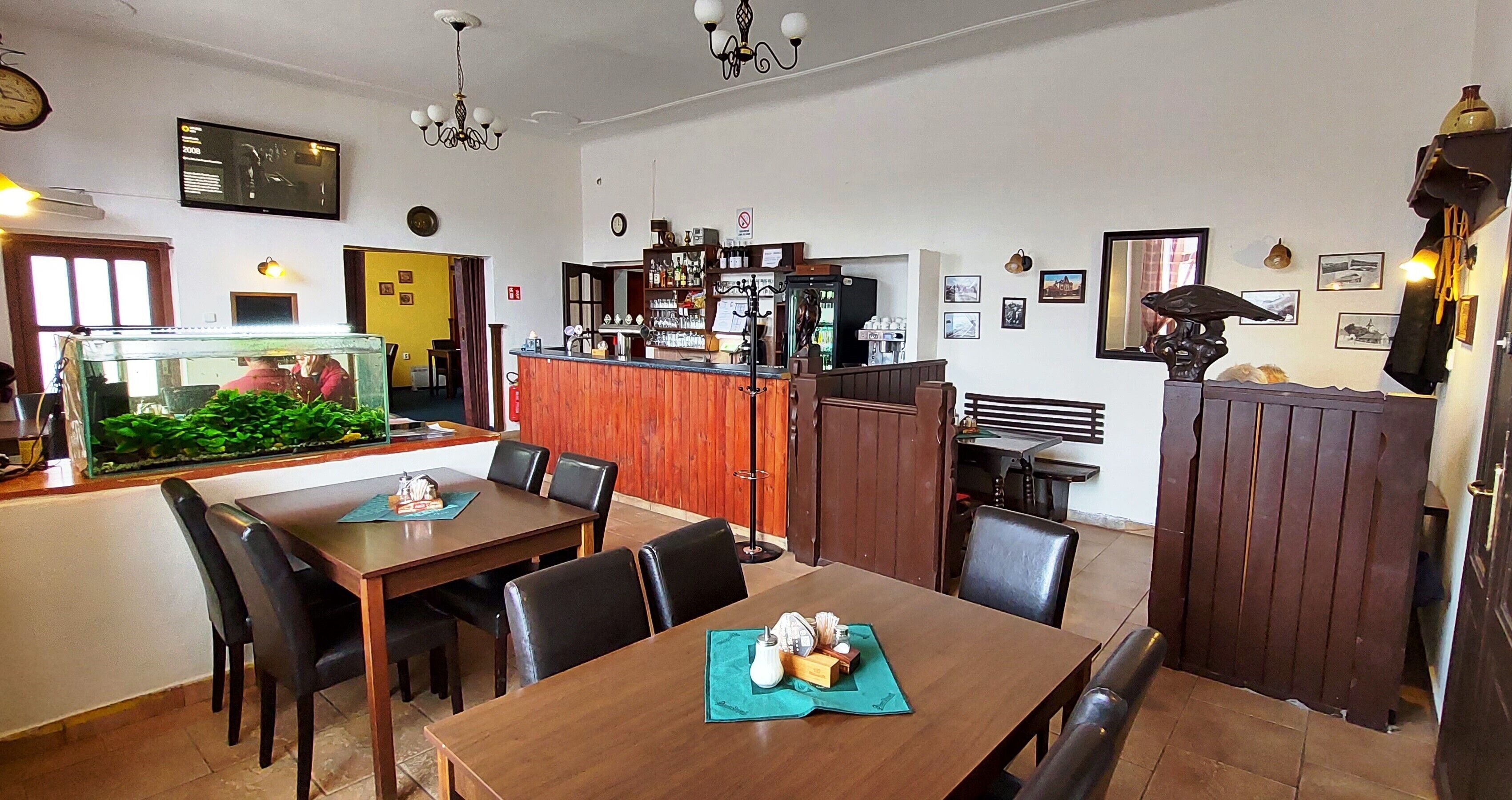 Ein Restaurant mit einem Holztisch, schwarzen Stühlen, einem Aquarium, einer Bar mit einem Kühlschrank und verschiedenen Wanddekorationen.