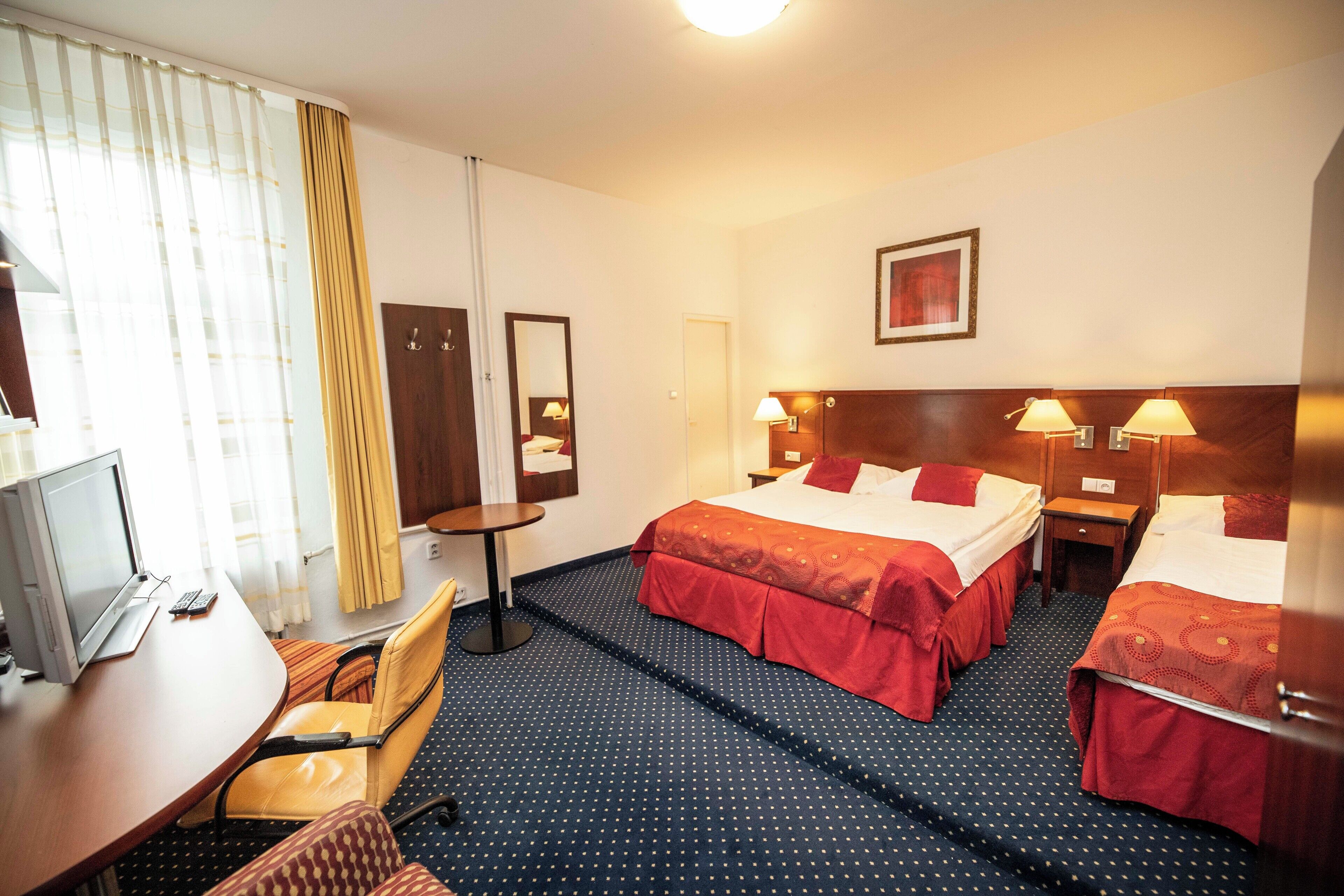 A hotel room with two beds, a desk with a laptop, a chair, and a small table.