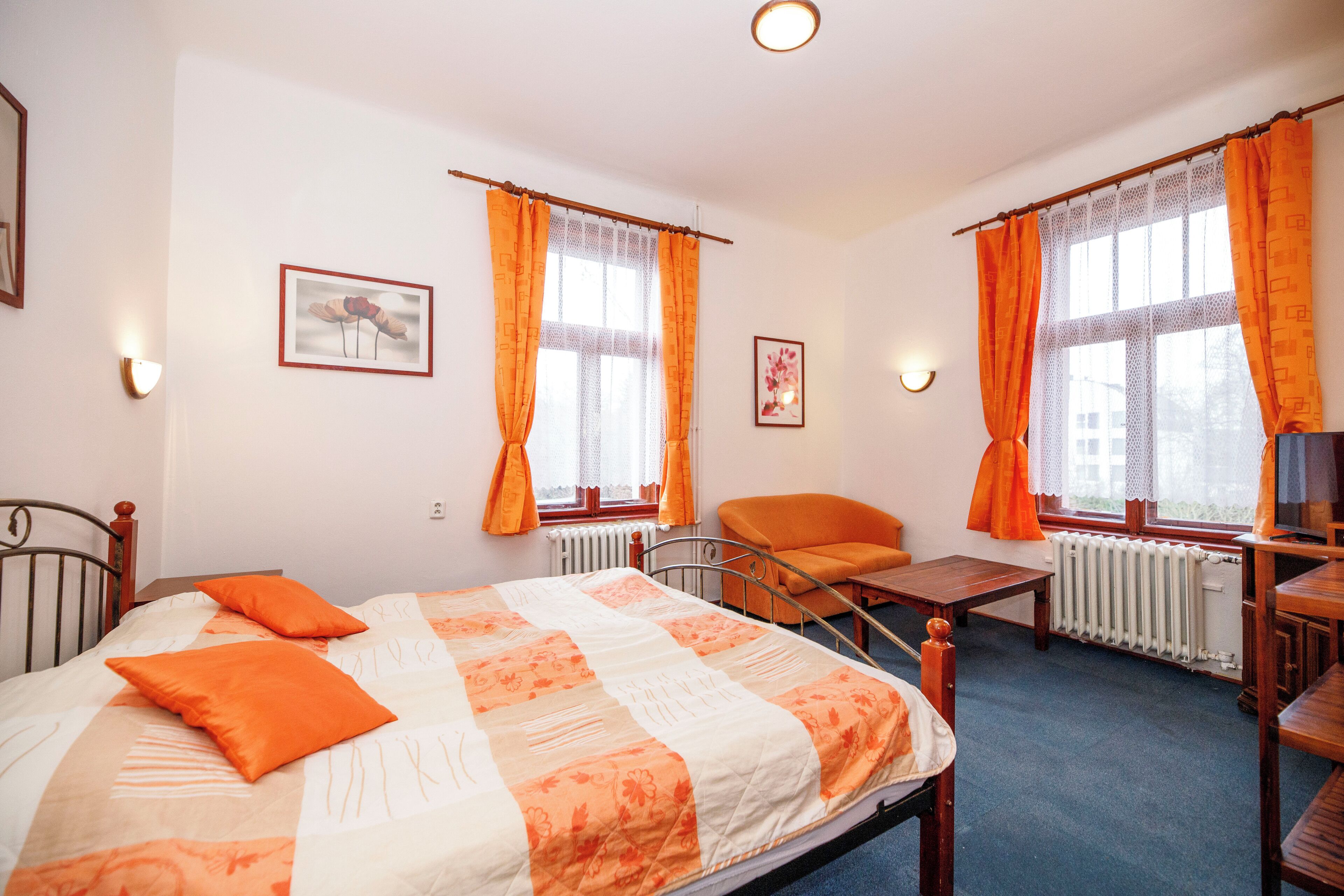 A bedroom with a bed, two chairs, a table, and two windows with curtains.