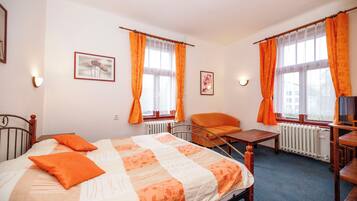 A bedroom with a bed, two chairs, a table, and two windows with curtains.