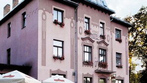 A pink building with a sign reading "Grand Hotel" and a stone wall with yellow fencing.