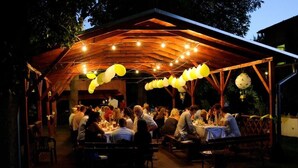 An outdoor dining area with tables under a wooden pergola, string lights, and balloons.