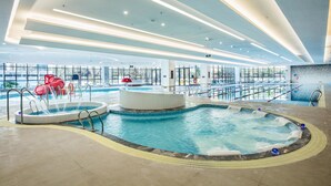 Una piscina interior moderna con hidromasaje, tobogán acuático y tumbona.