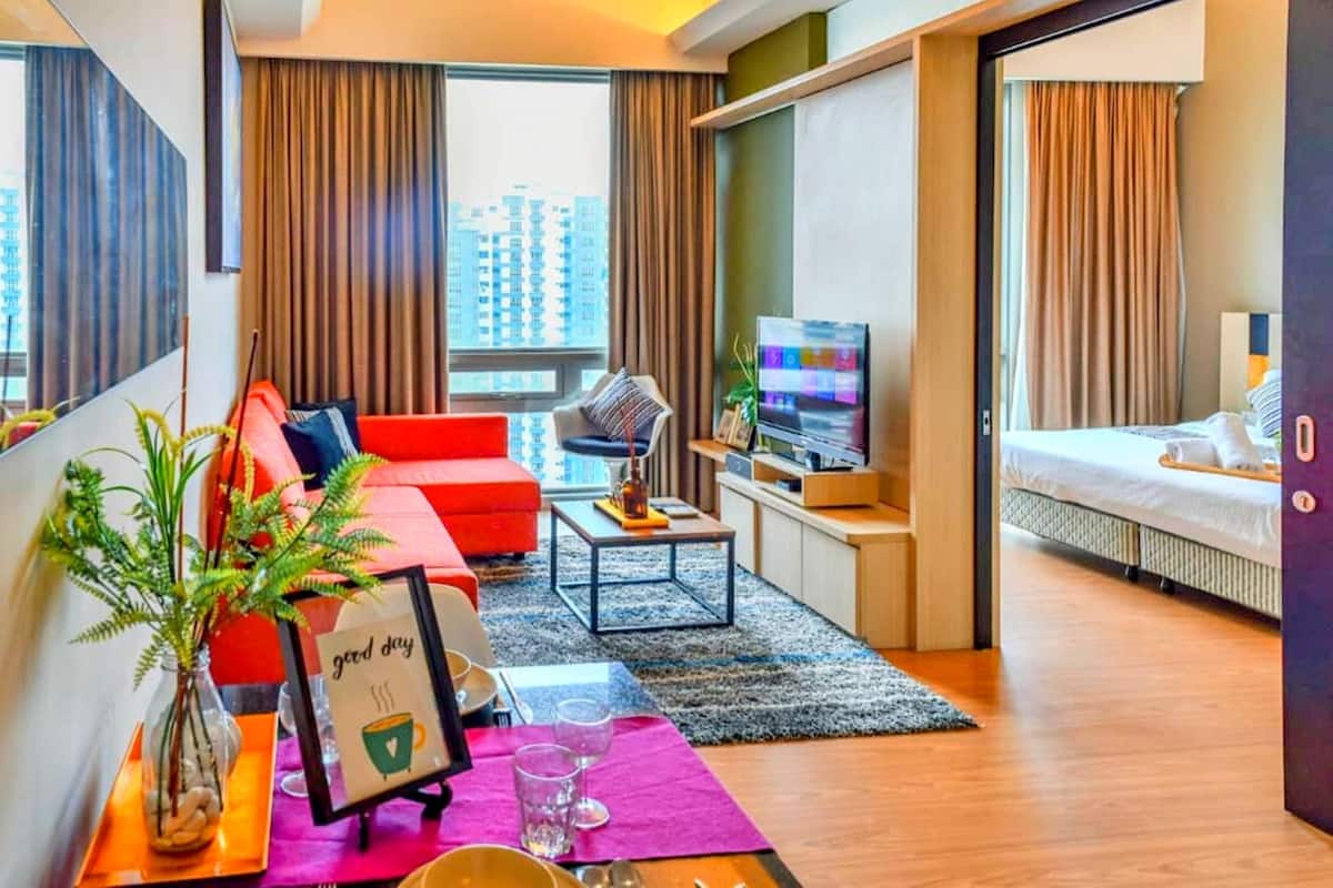 A modern hotel room with a red sofa, a small coffee table, a TV, and a bed.