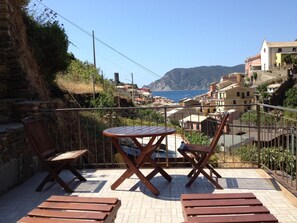 A terrace with wooden furniture, a view of a coastal town, and a mountainous backdrop. - Camere Giuliano (Vernazza)