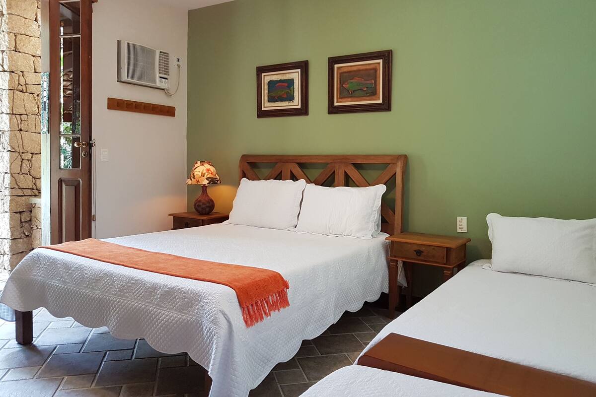 A room with two beds, a wooden headboard, a wall-mounted air conditioner, and two framed pictures.
