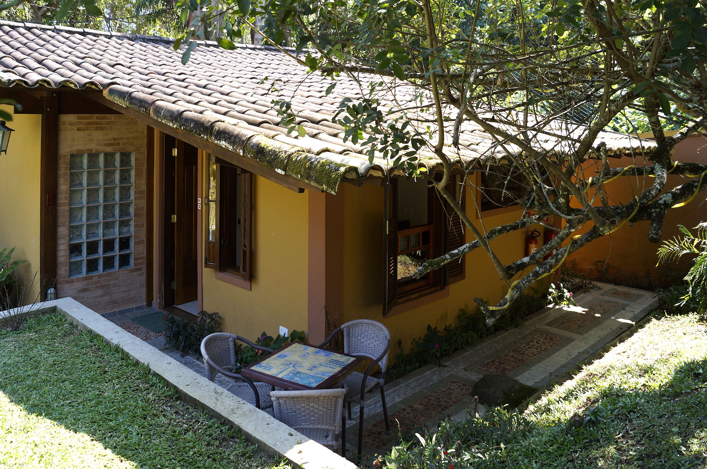 A yellow building with a tiled roof, a window, and a door. There is a table and two chairs outside.