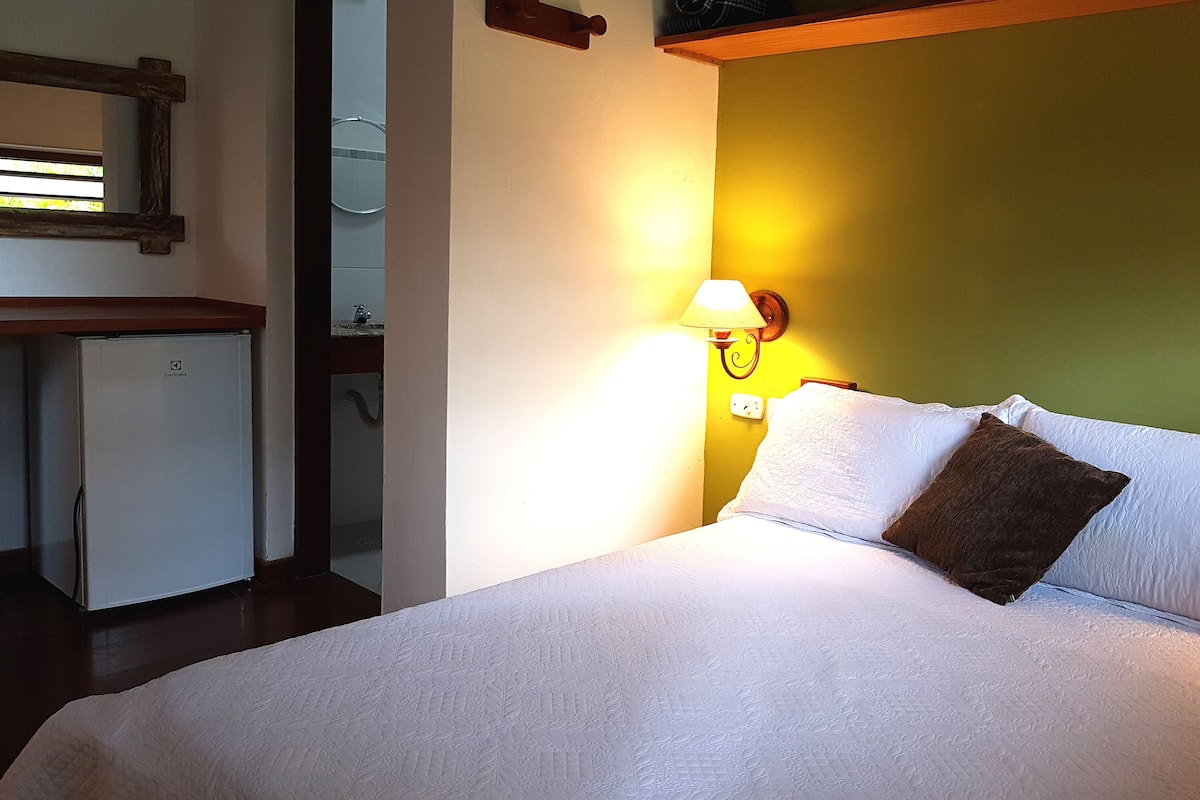 A bedroom with a bed, a nightstand, a lamp, and a small refrigerator.