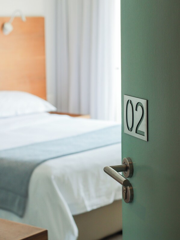 A hotel room with a bed, a door with the number 02, and a window with curtains.