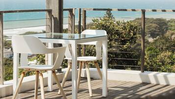 Un balcón con una mesa de vidrio y dos sillas blancas, con vistas a la costa.