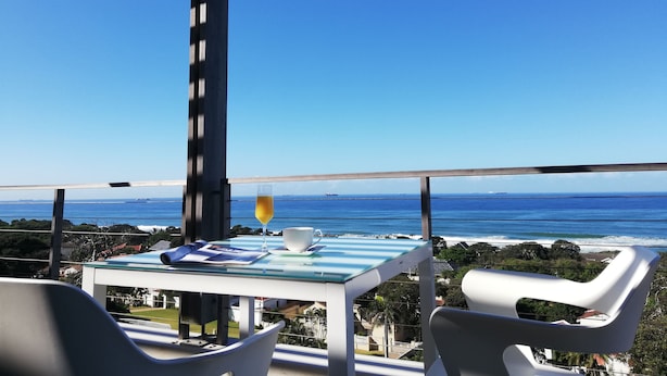 A balcony with a table, chairs, and a glass of orange juice. - Ocean Vista Boutique Guest House (Umhlanga)