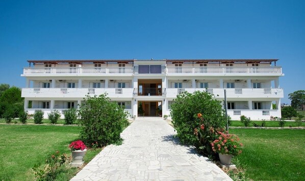 A multi-story building with a central entrance, surrounded by well-maintained lawns and potted plants.