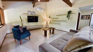 A living room with a TV, sofa, and blue armchair. - Pousada Morro das Palmeiras (Imbituba)