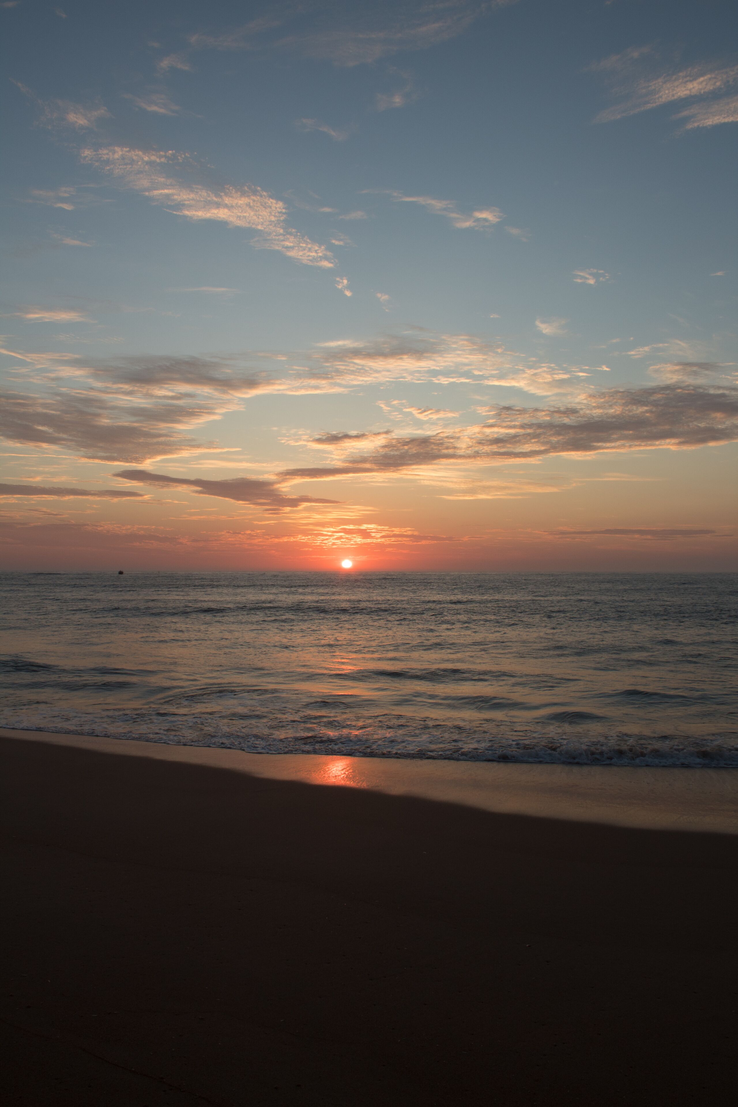 A sunset over the ocean with a beach in the foreground.