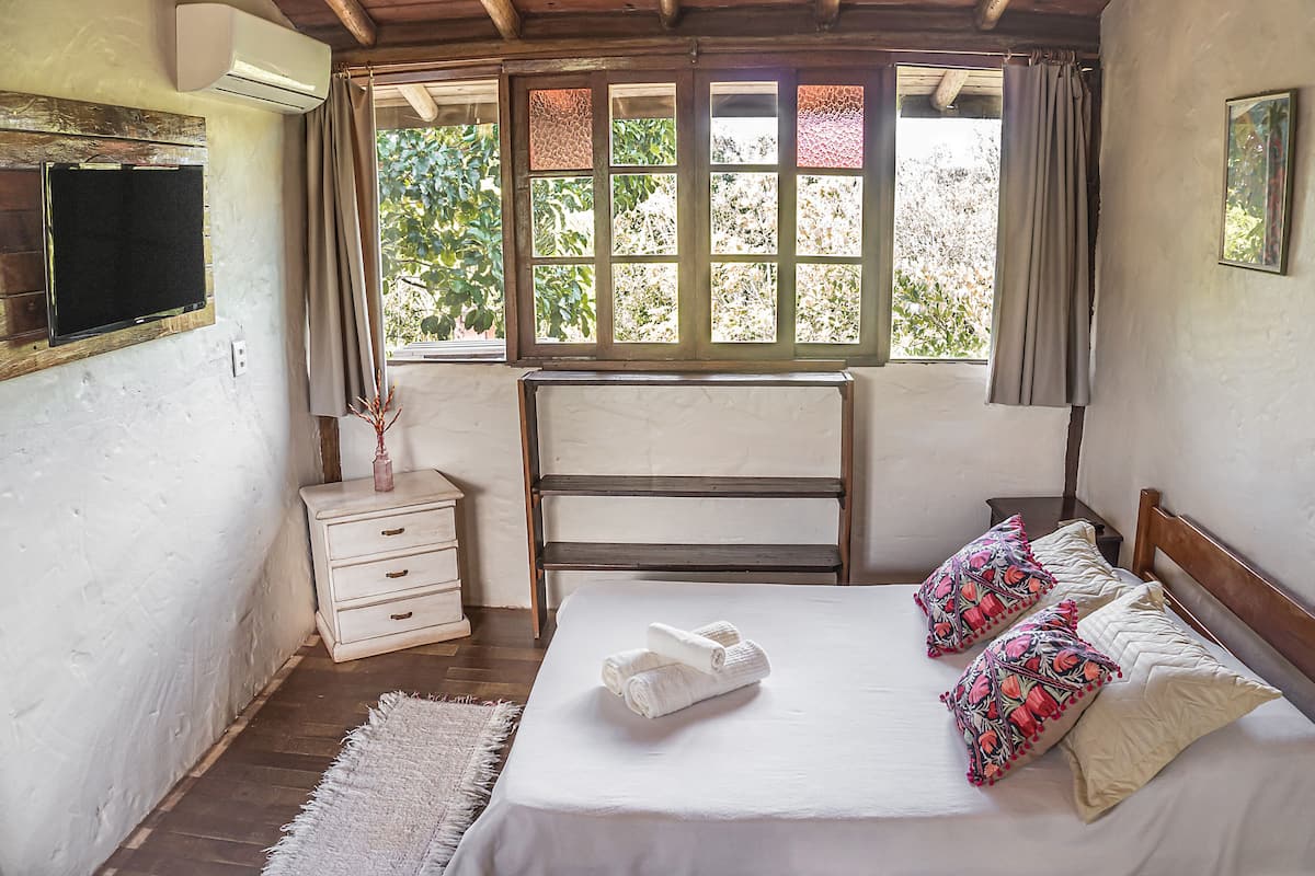 Ein Schlafzimmer mit Bett, Nachttisch, Fernseher und einem Fenster mit Vorhängen.