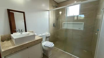 Un baño moderno con ducha envuelta en cristal, lavamanos blanco y un inodoro.