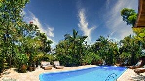 A swimming pool surrounded by lush greenery and lounge chairs. - Pousada Morro das Palmeiras (Imbituba)