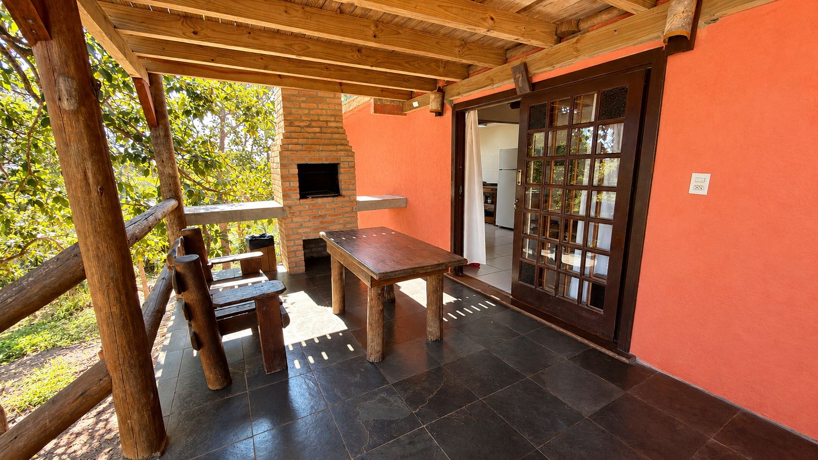 Un patio exterior con chimenea de ladrillo, muebles de madera y vistas al entorno verde.