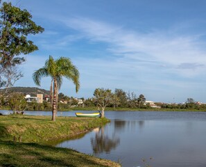 A calm lake with a boat, palm trees, and houses in the background. - Pousada Morro das Palmeiras (Imbituba)
