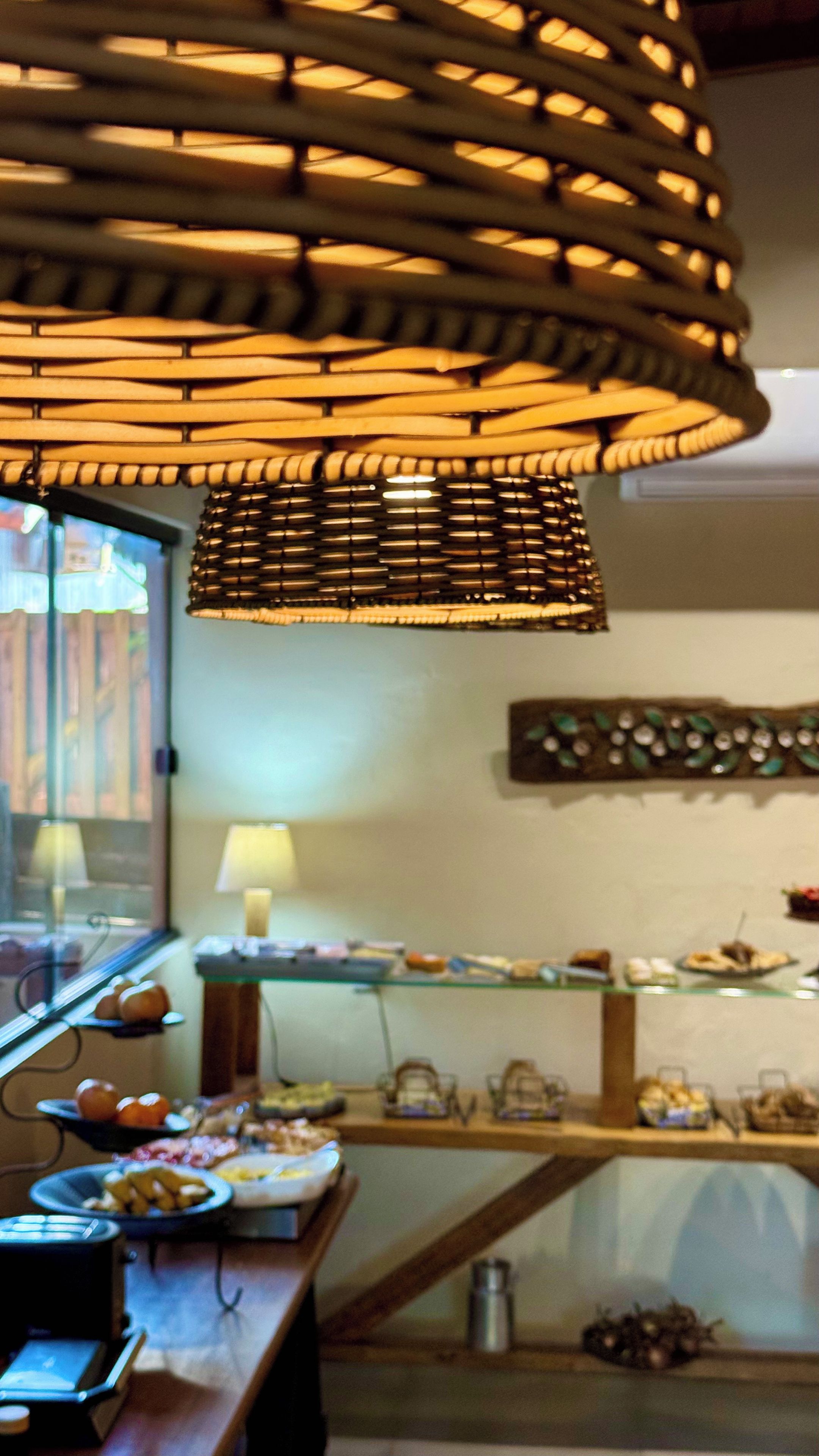 A room with a hanging light fixture, a window with blinds, and a buffet table with various food items.
