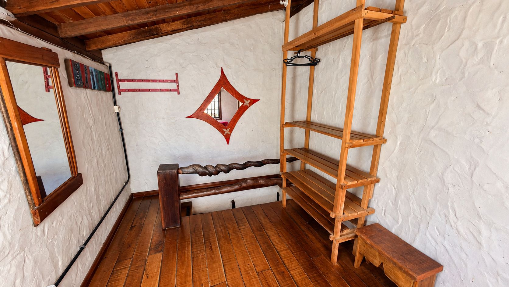 A room with wooden flooring, a bench, a wooden shelf unit, and a wall-mounted mirror.