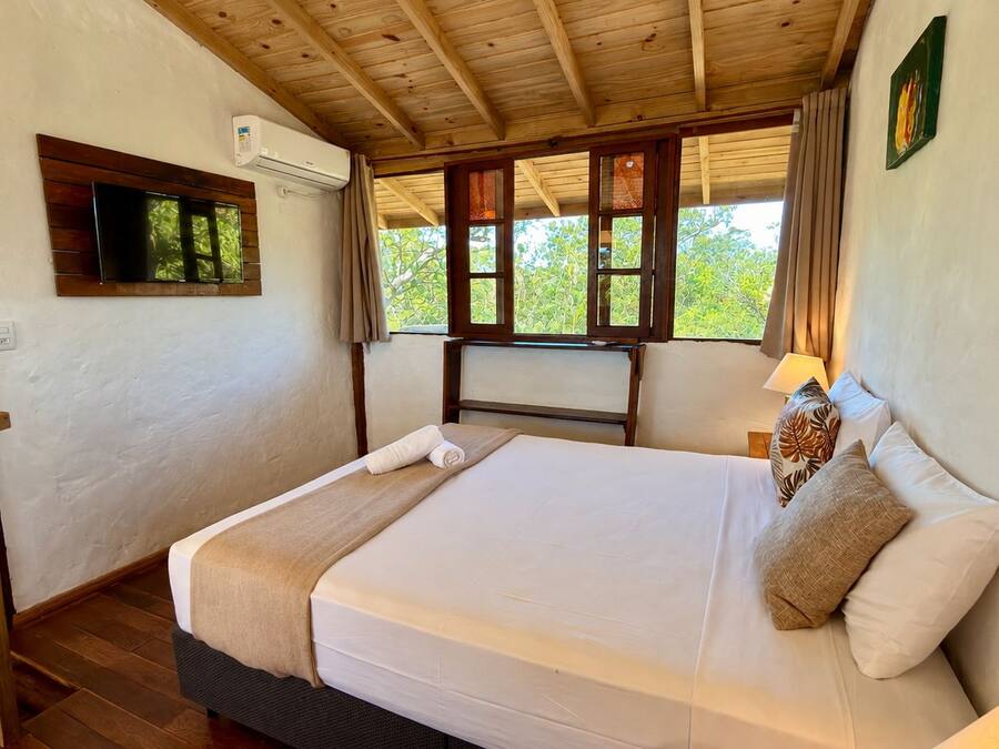 Una cama individual con cabecera de madera, una lámpara de noche y una ventana con cortinas.