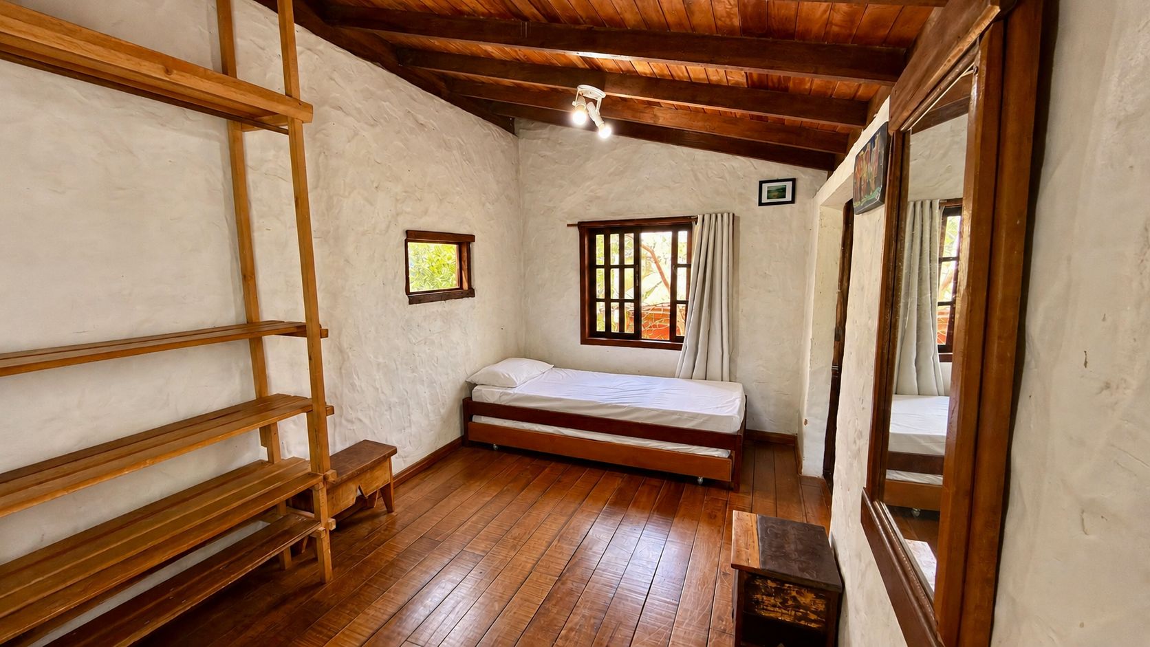 Ein Zimmer mit Holzboden, einem Bett, einem Fenster mit Vorhängen und einer Holzleiter.
