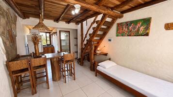 Una habitación rústica con una mesa de comedor de madera, sillas, una cama individual y una escalera.