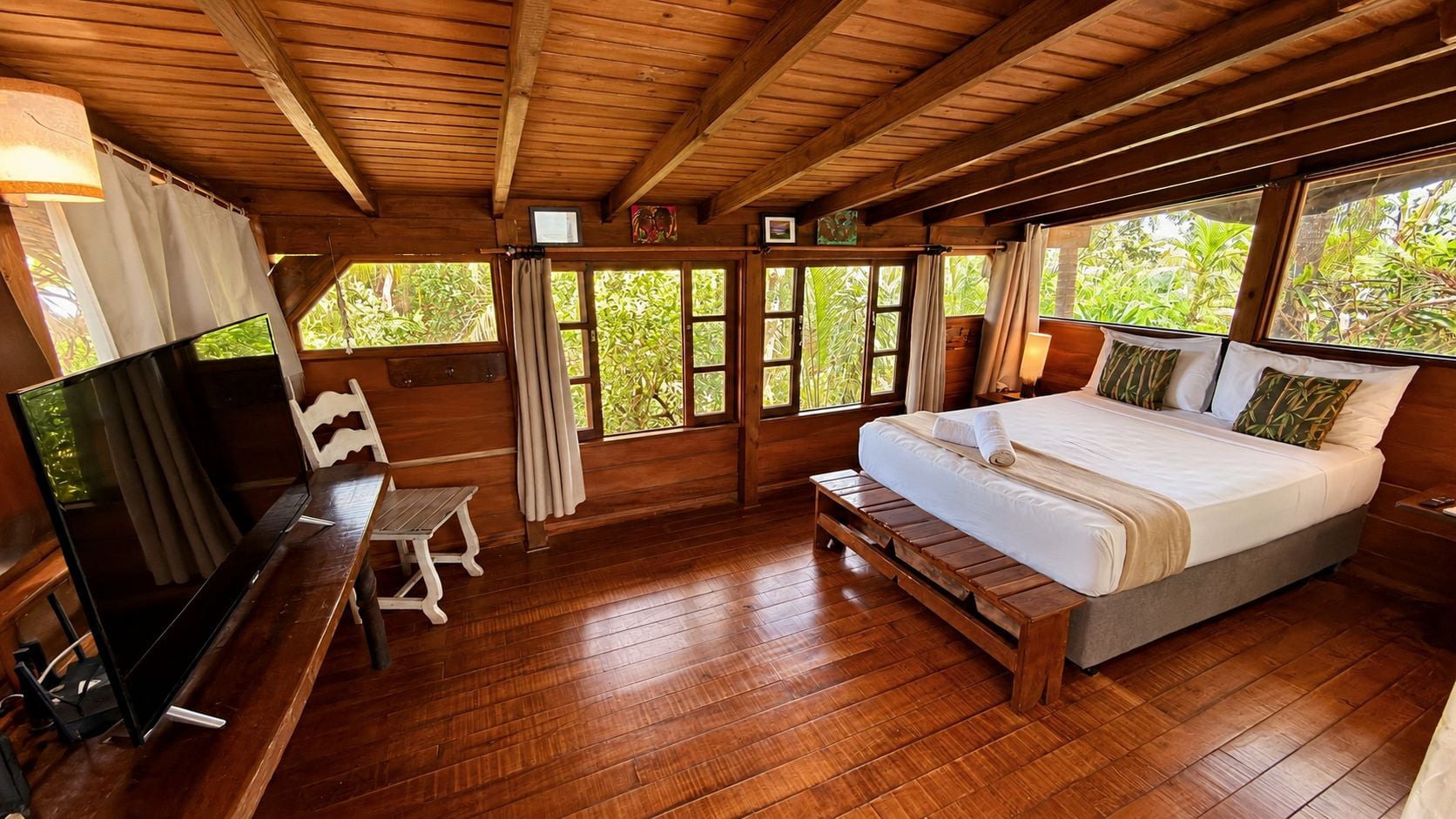 A wooden-floored room with a bed, a television, and a bench.