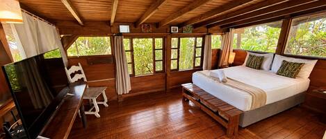 Una habitación con suelo de madera, una cama, un televisor y un banco.