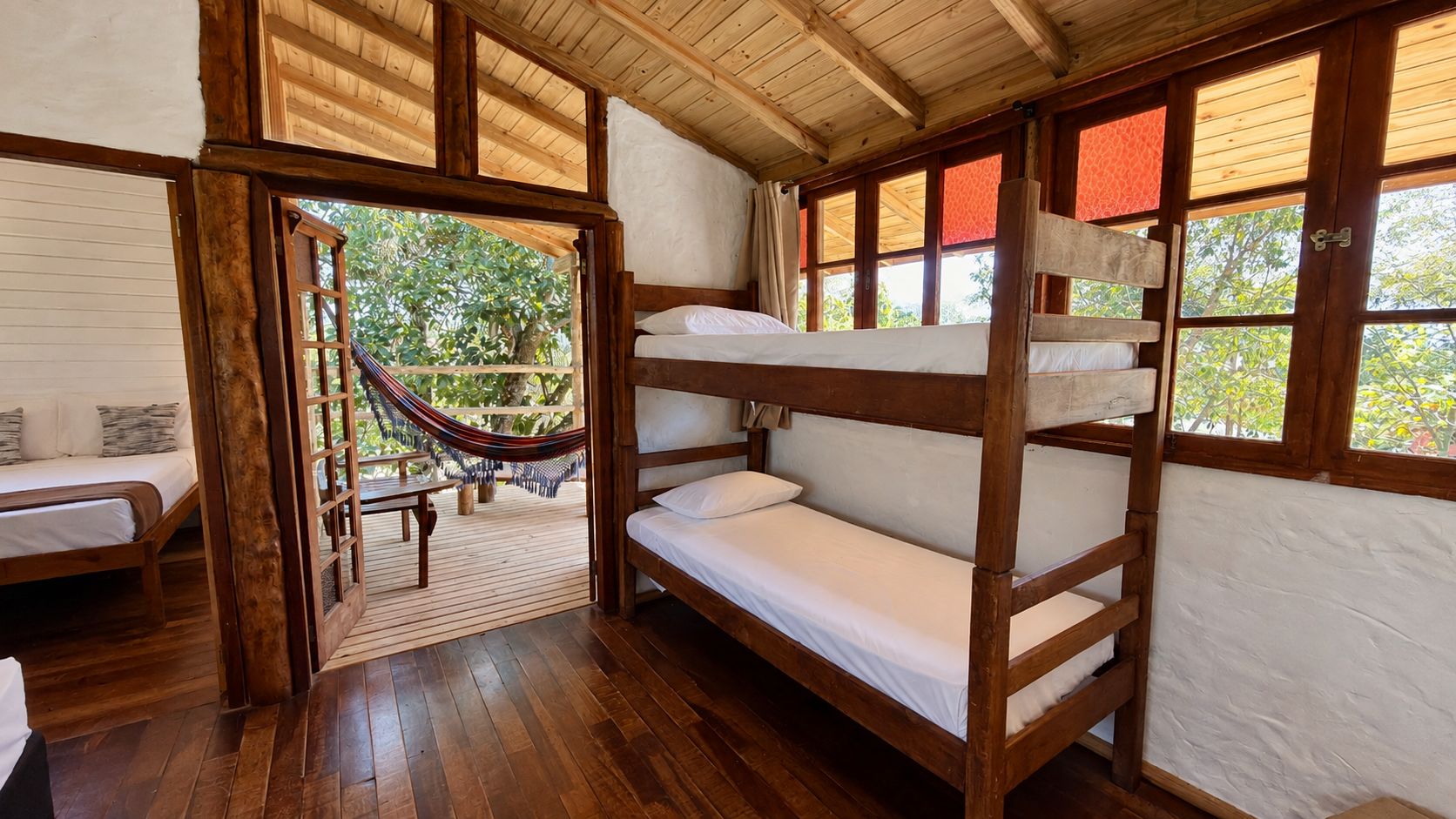 Quarto de madeira com beliches, uma rede e vista para o verde lá fora.