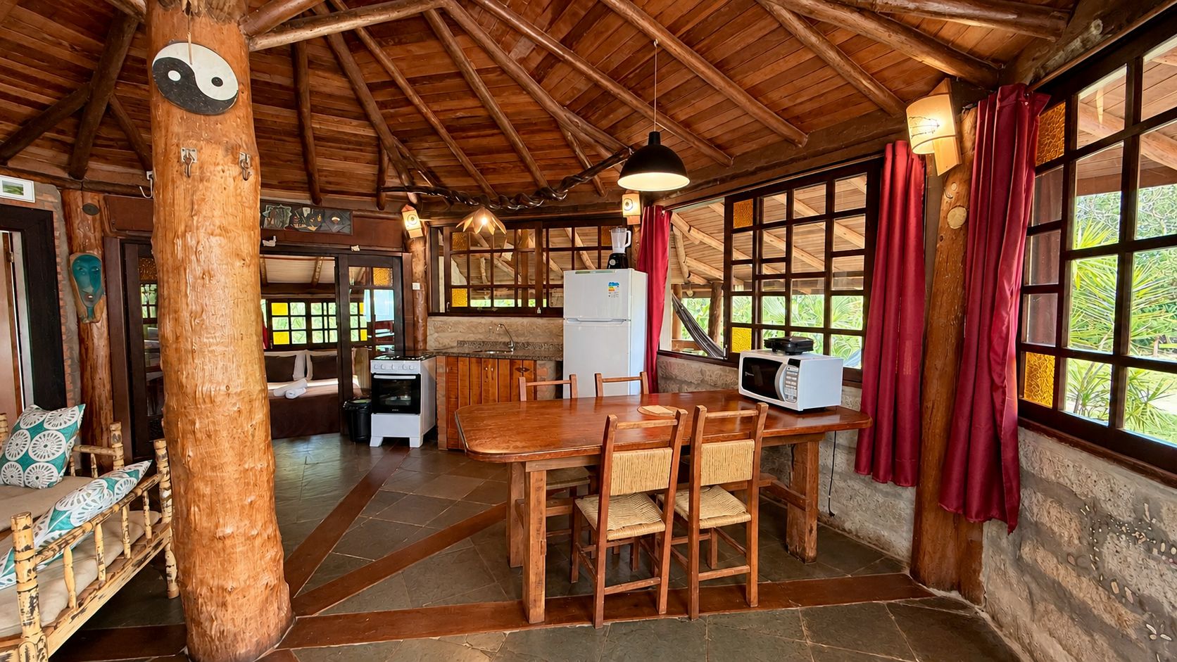 Interior rústico em madeira com área de jantar, cozinha e janelas amplas.