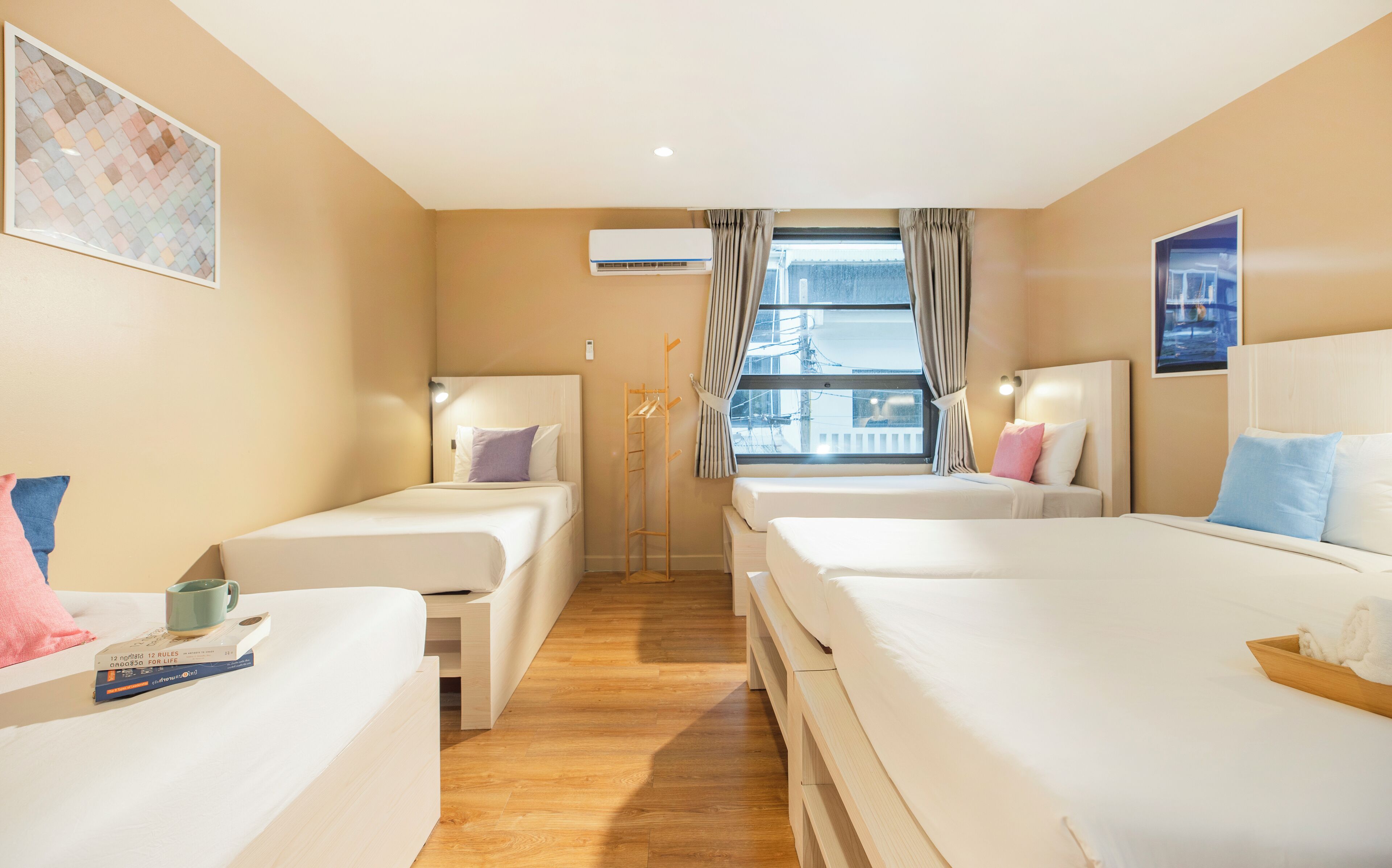 Hotellihuone, jossa on kaksi erillistä sänkyä, puulattia, ikkuna verhoilla ja ilmastointilaite.