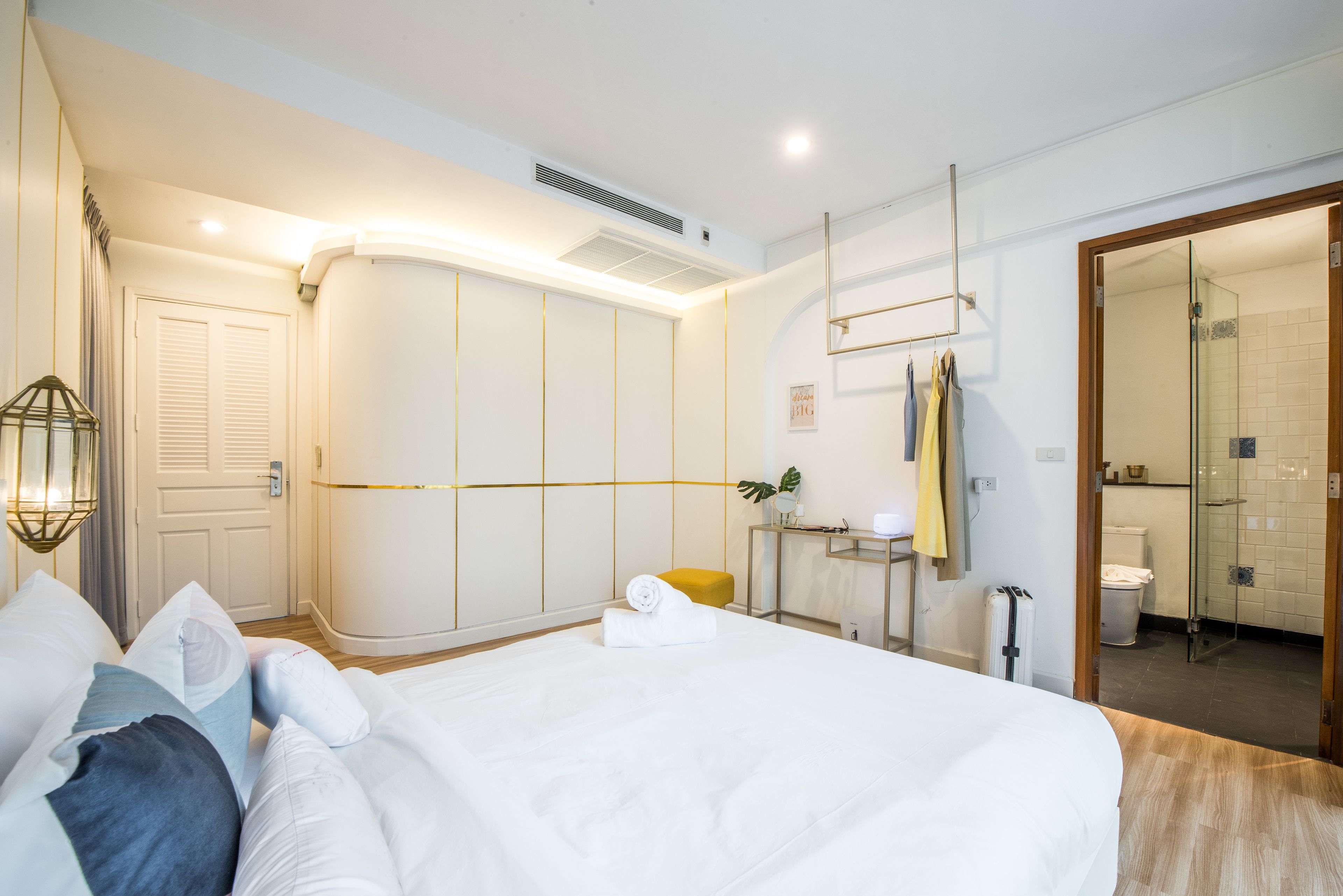 A modern hotel room with a large bed, a bedside table, a mirror, and a bathroom visible through an open door.