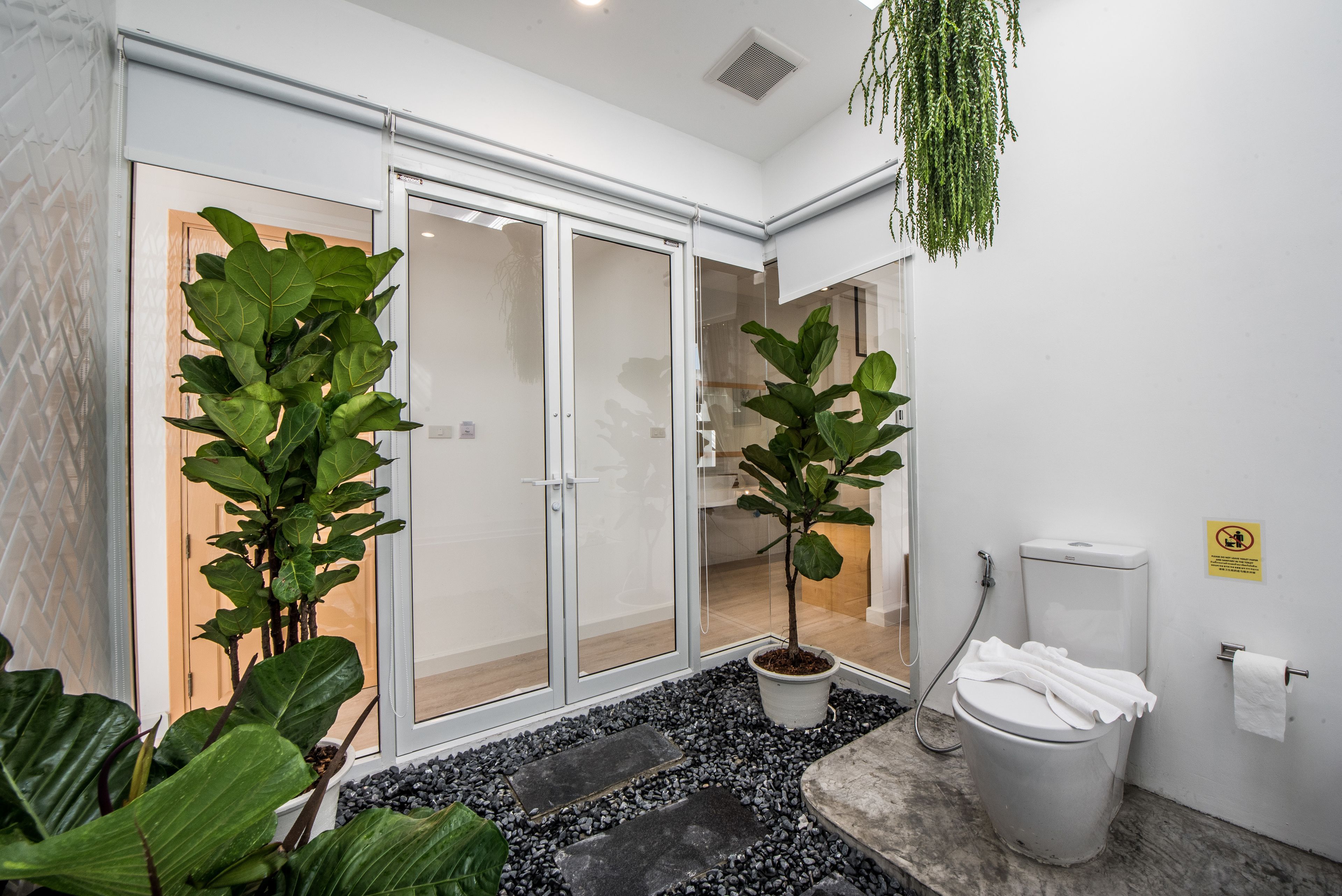 A modern bathroom with a glass shower enclosure, a toilet, and potted plants.