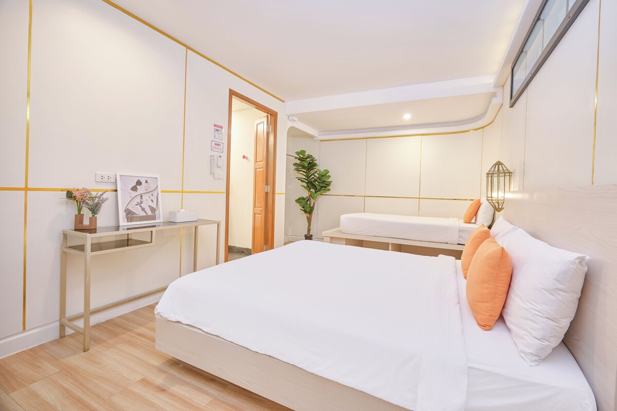 A modern bedroom with a large bed, bedside tables, a desk, and a potted plant.