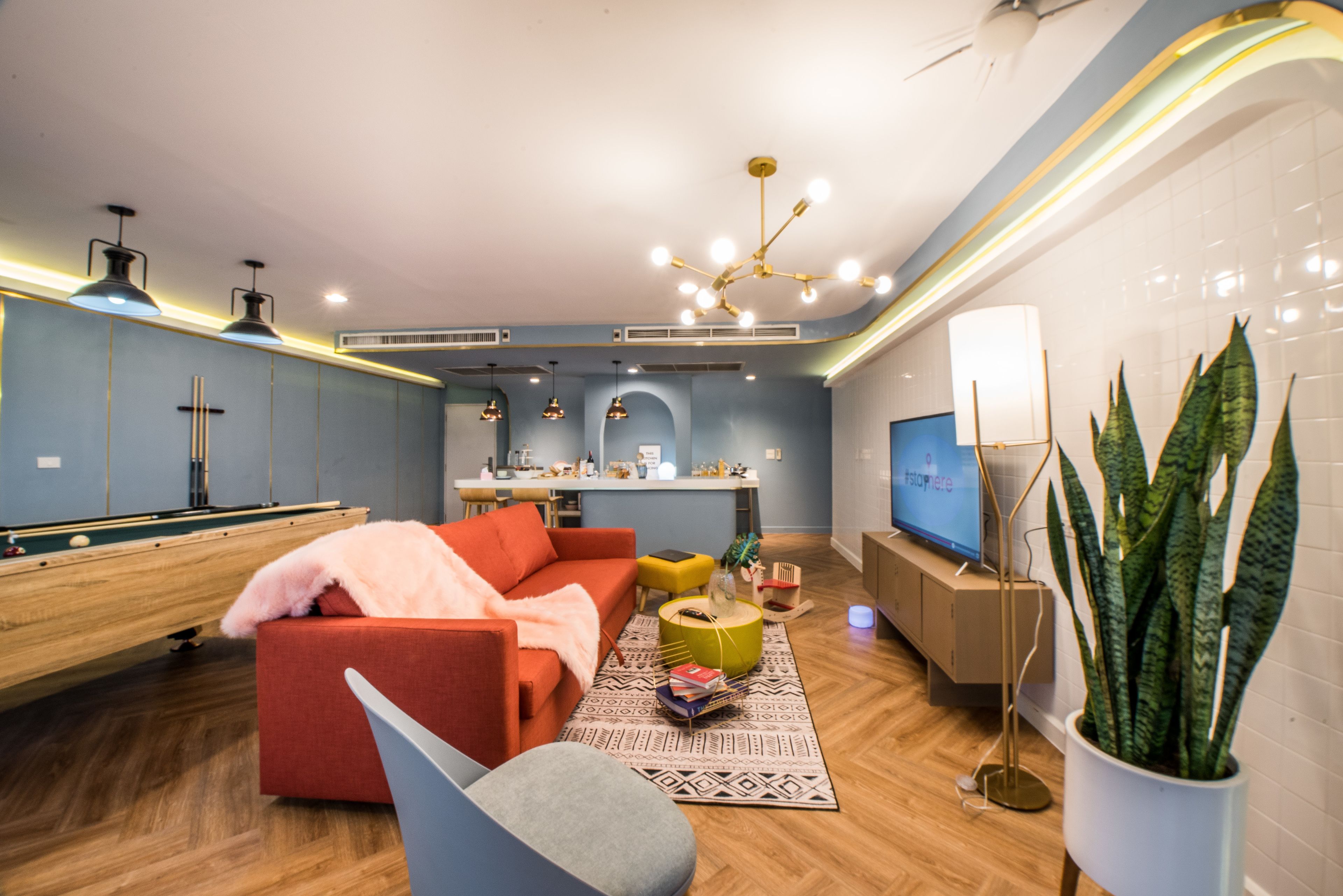 A modern living room with a pool table, a red sofa, a television, and a potted plant.