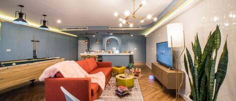 A modern living room with a pool table, a red sofa, a television, and a potted plant.