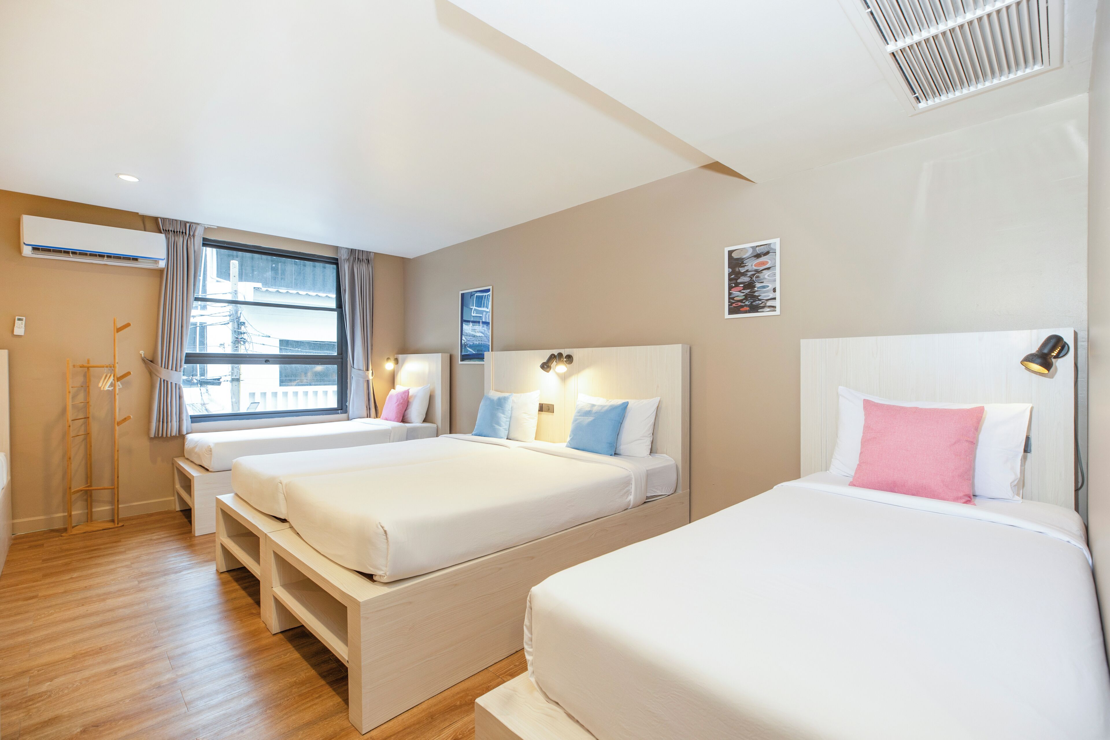 Hotelkamer met twee bedden, een raam met gordijnen, een nachtkastje, een lamp en een wandairconditioner.