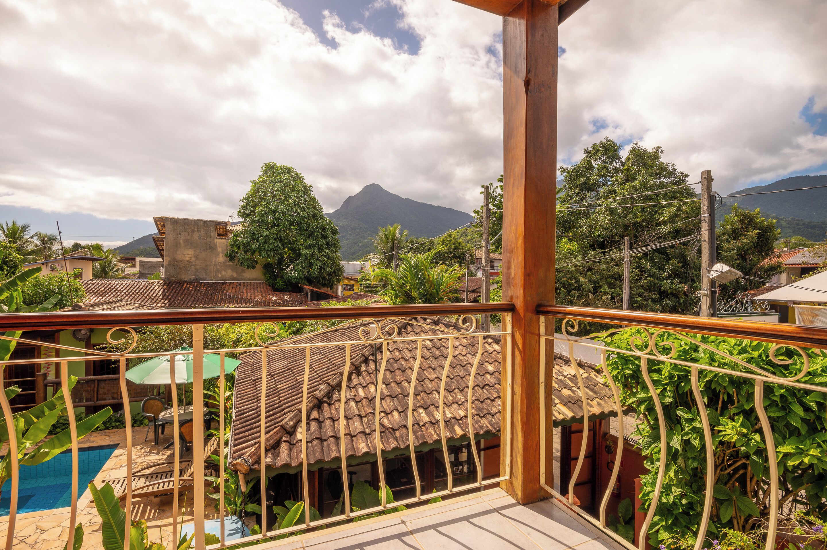 Ein Balkon mit Blick auf einen Berg, ein Schwimmbad und üppiges Grün.
