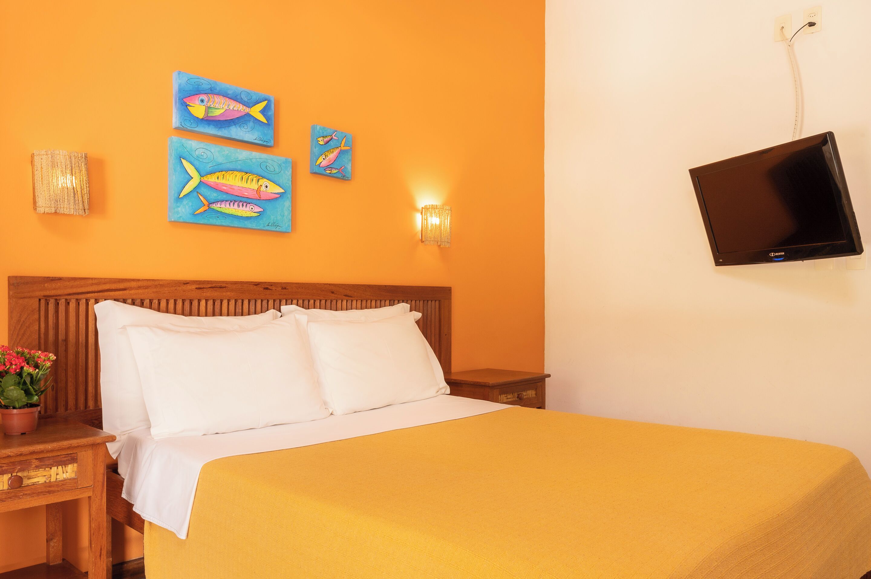 A hotel room with a bed, a wooden headboard, a flat-screen TV mounted on the wall, and artwork depicting fish.