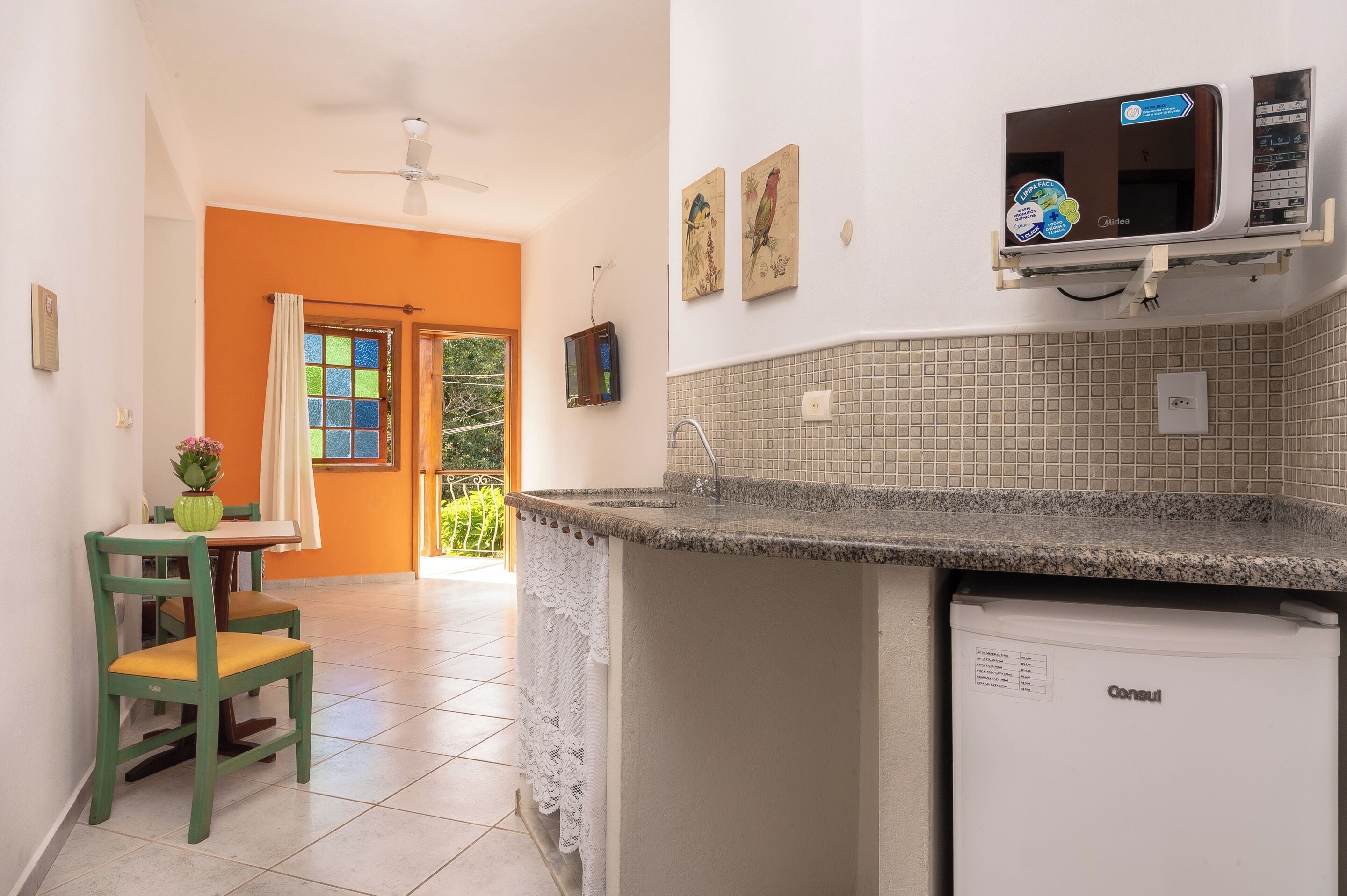 A kitchen with a built-in microwave, a small refrigerator, and a dining area with a chair and table.