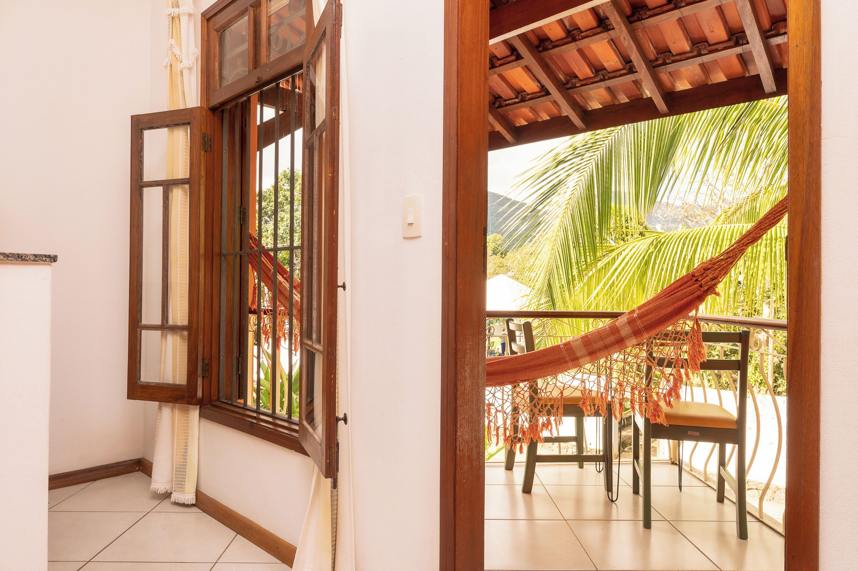 A room with a wooden door leading to a balcony with a hammock and chairs.