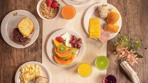 A wooden table set with breakfast items including toast, eggs, fruit, and beverages. - Pousada Atiaia (Ilhabela)