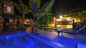 A pool area with lounge chairs and a hot tub, surrounded by potted plants and a building with a tiled roof. - Pousada Atiaia (Ilhabela)