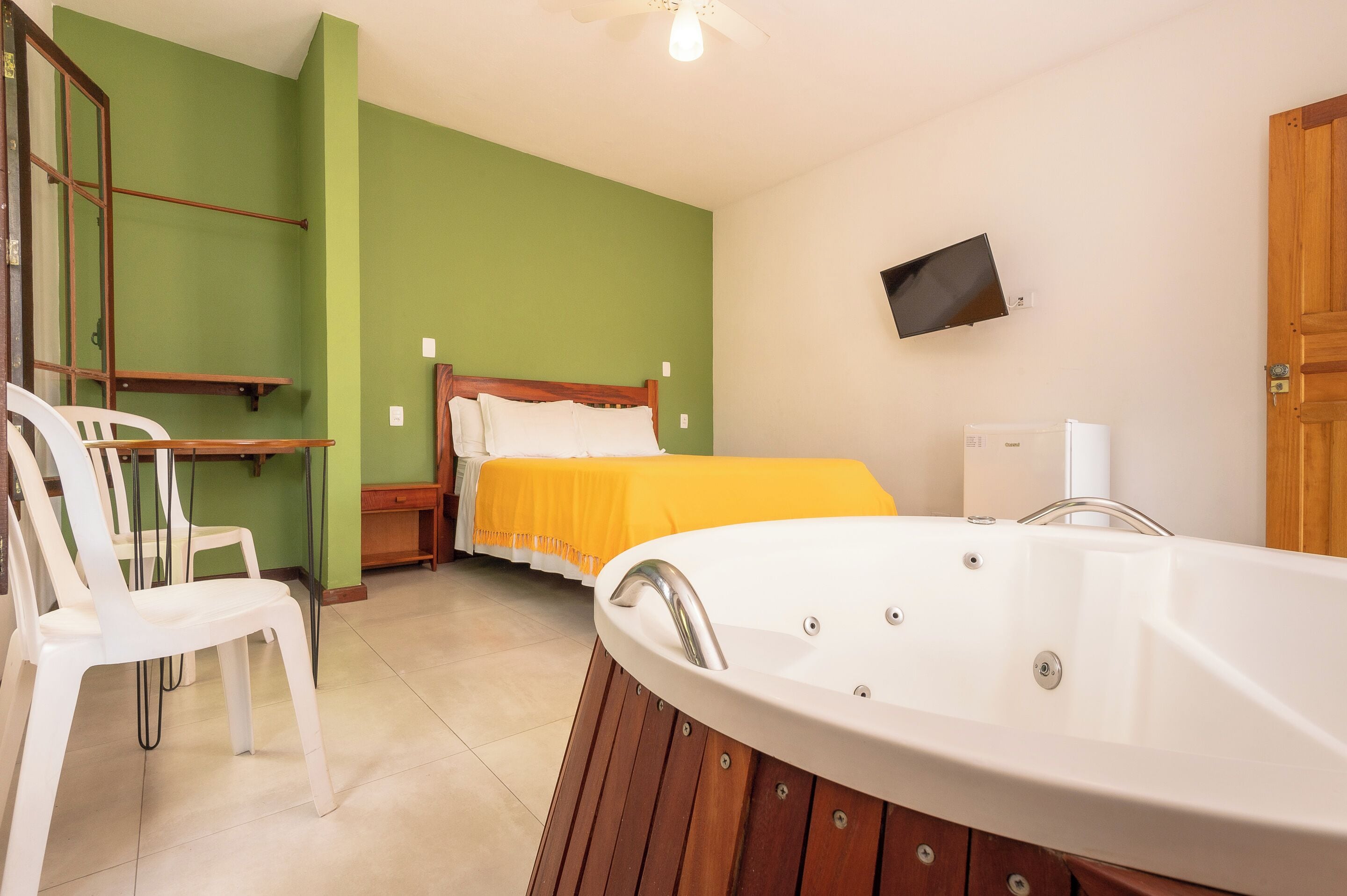 A room with a bed, a white bathtub, a television on the wall, and a chair.