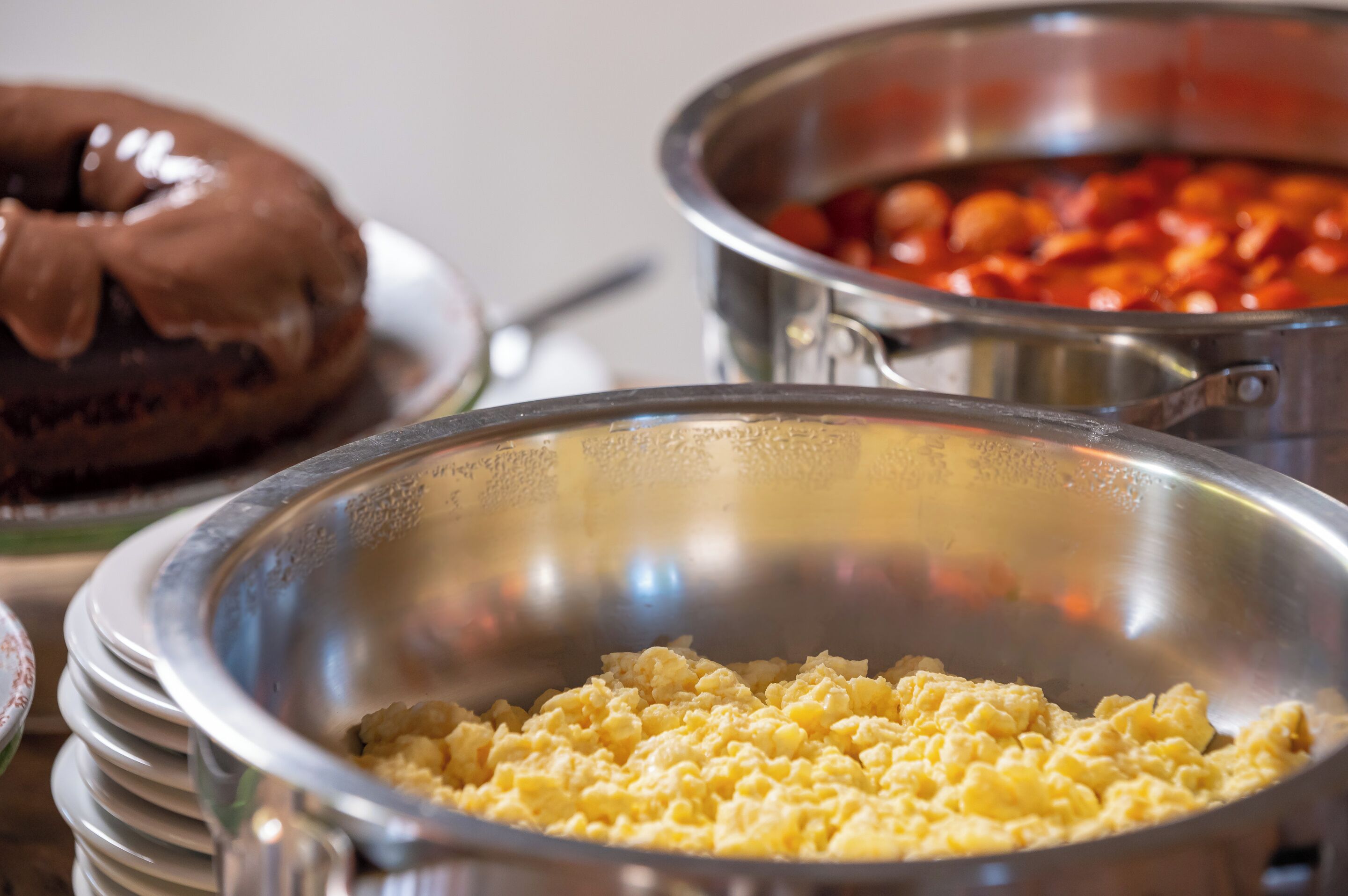 A buffet with scrambled eggs, a chocolate-glazed donut, and a pot of red beans.